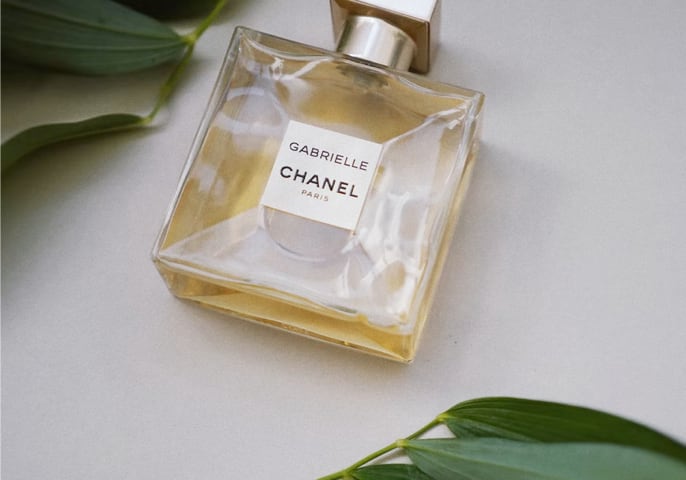 A bottle of Gabrielle Essence Eau De Parfum, surrounded by leaf sprigs